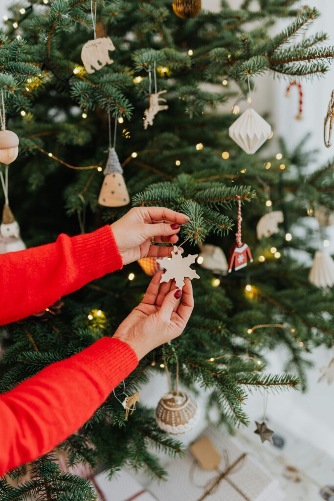 Hands decorating a Christmas tree with a snowflake ornament, capturing a festive holiday spirit.
